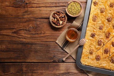 Photo of Delicious baklava with walnuts in baking pan, honey and nuts on wooden table, flat lay. Space for text