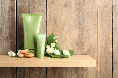 Photo of Tubes of cosmetic products, almond nuts and flowers on shelf near wooden wall, space for text