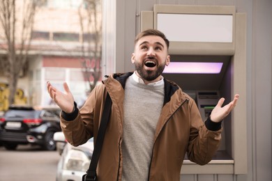 Photo of Excited young man near cash machine outdoors