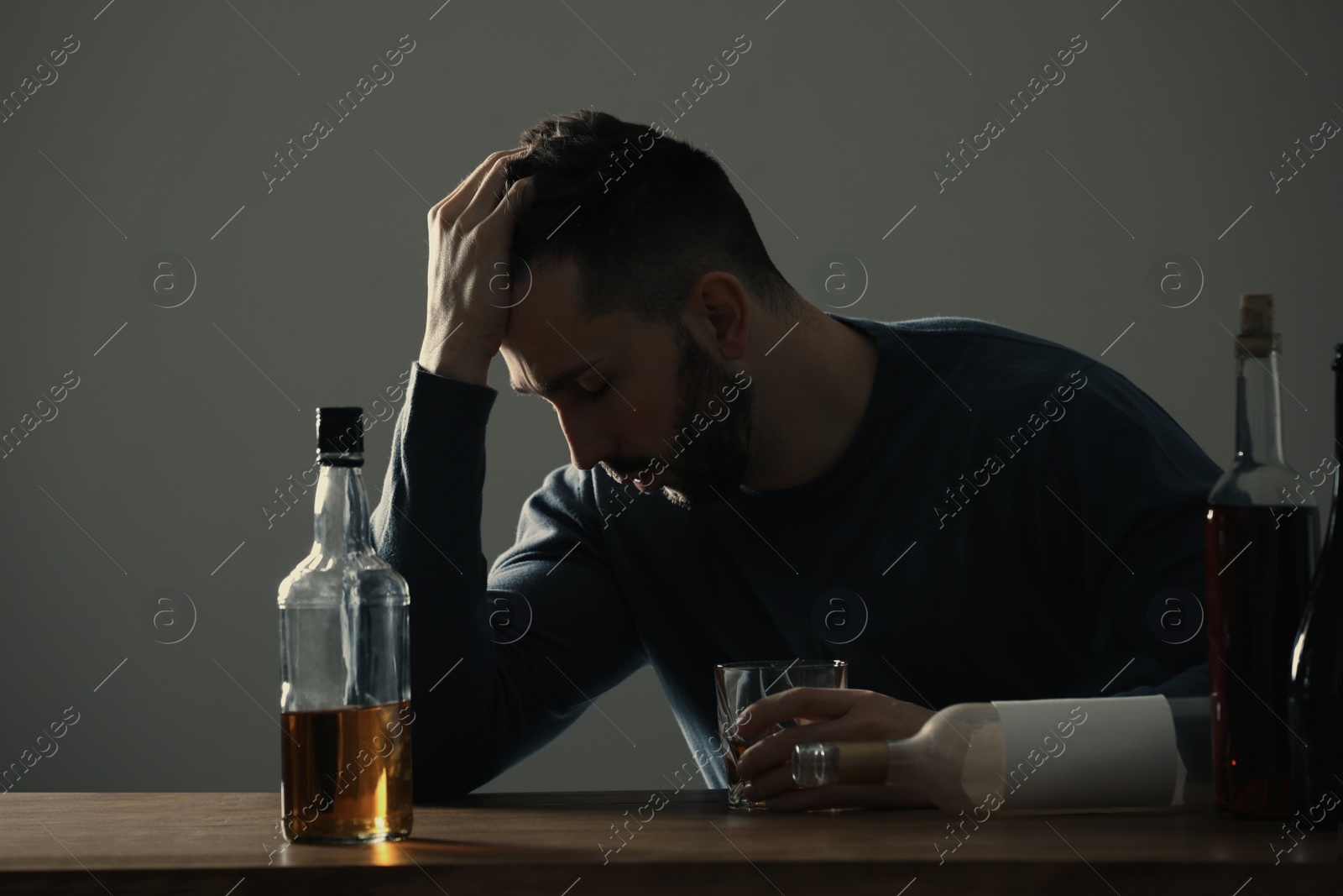 Photo of Addicted man with alcohol drink at wooden table indoors