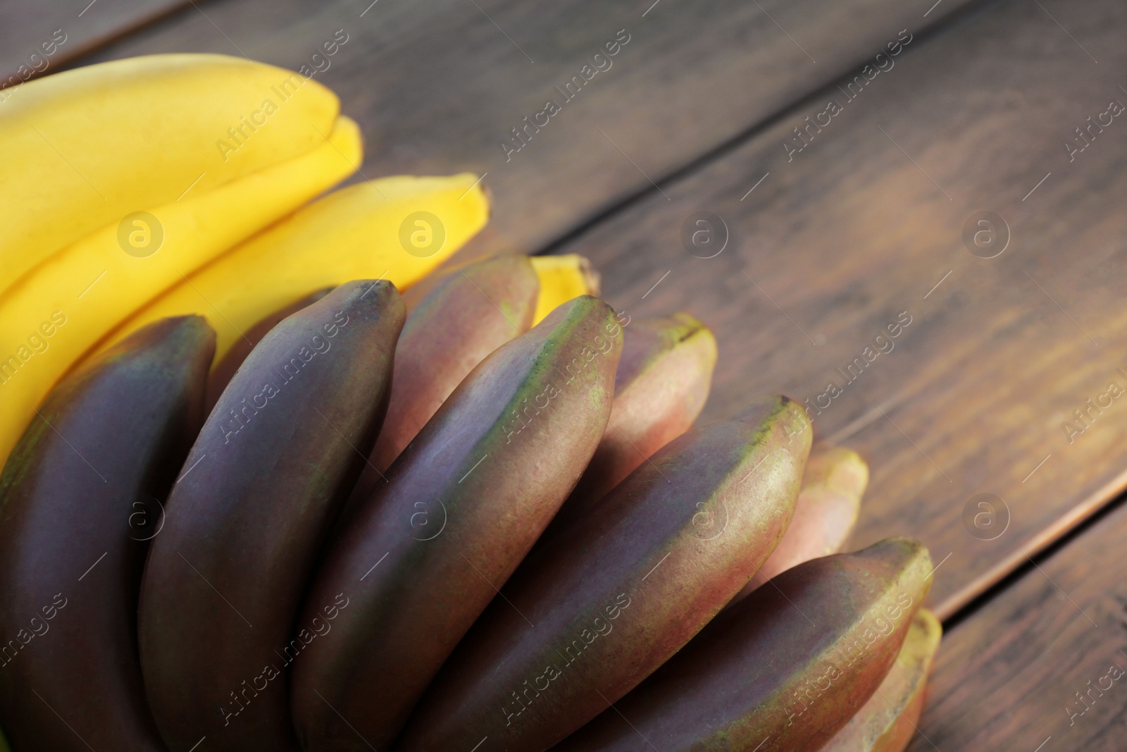 Photo of Tasty purple and yellow bananas on wooden table, closeup