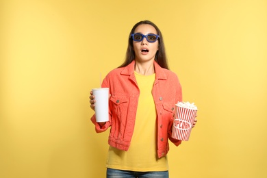 Photo of Emotional woman with 3D glasses, popcorn and beverage during cinema show on color background