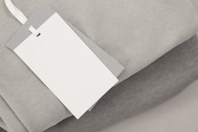 Photo of Garment with cardboard tag on beige background, closeup. Space for text