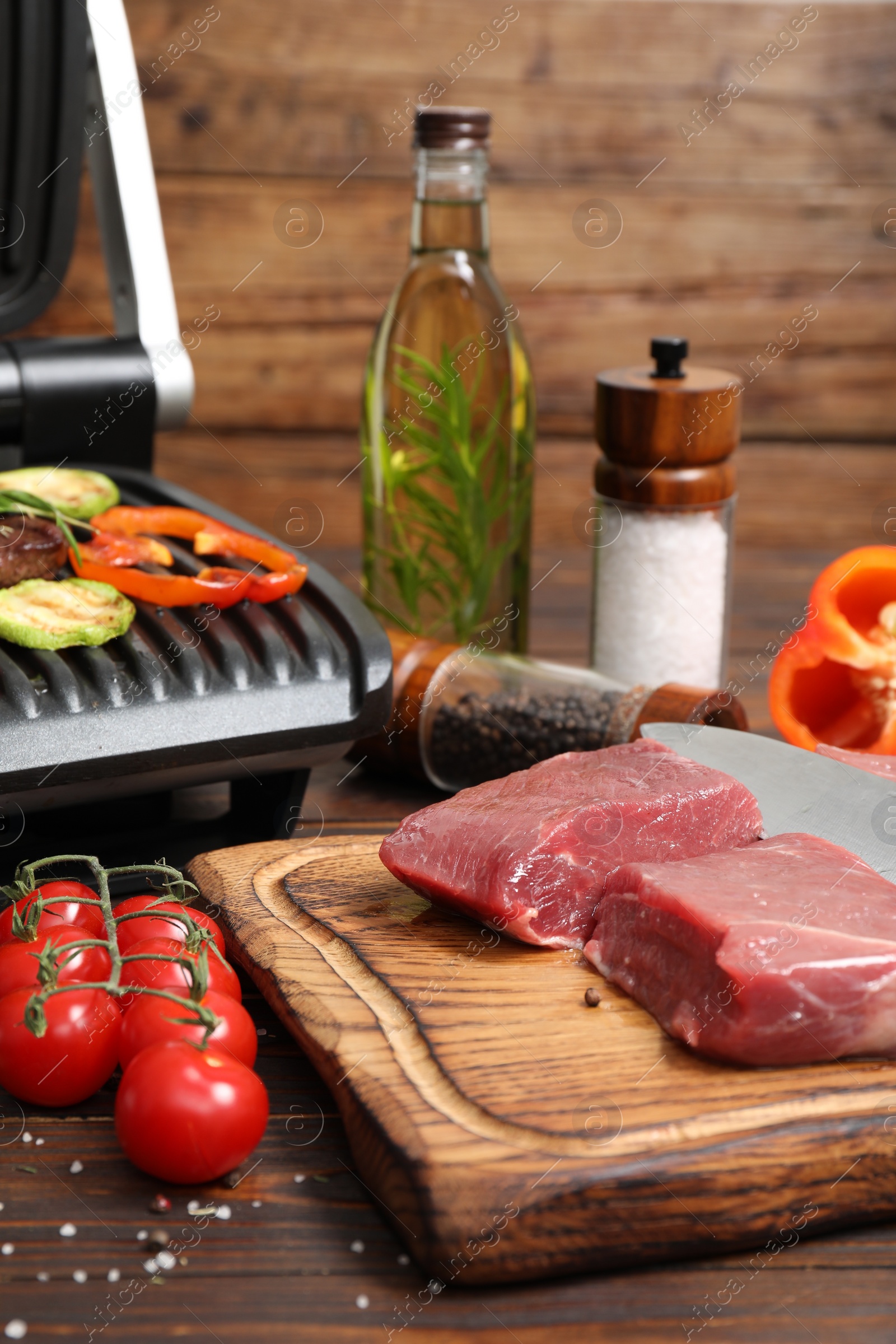 Photo of Electric grill with meat, spices and vegetables on wooden table