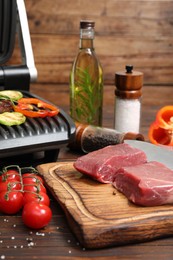 Photo of Electric grill with meat, spices and vegetables on wooden table