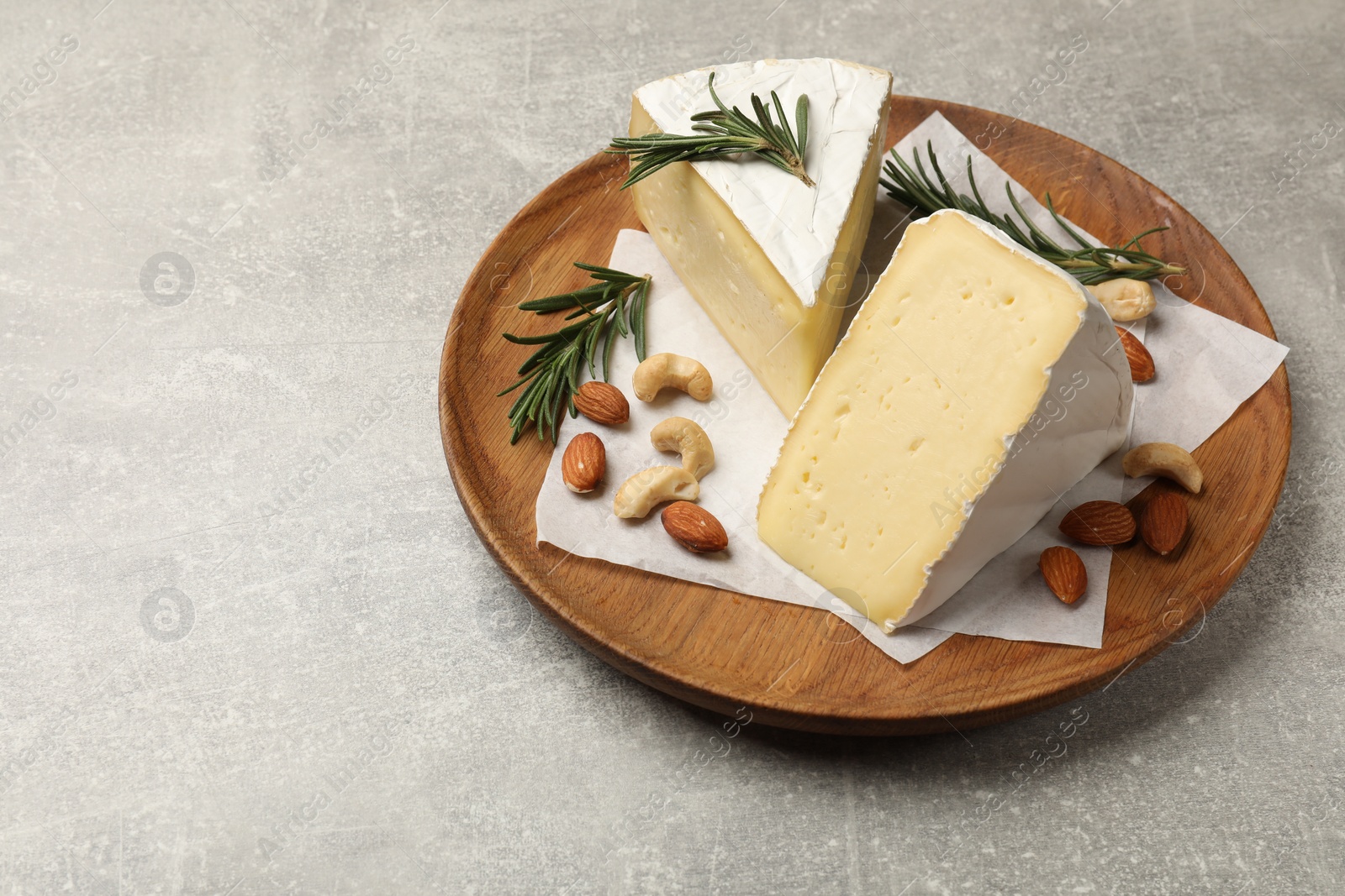 Photo of Plate with pieces of tasty camembert cheese, nuts and rosemary on grey textured table. Space for text