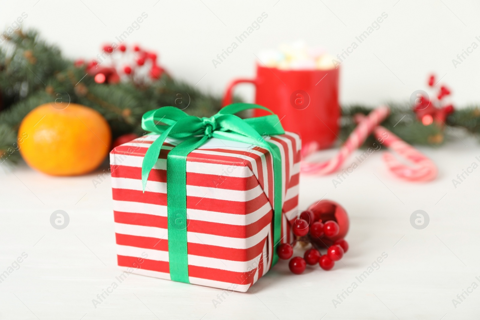 Photo of Christmas gift box and red berries on white table, closeup