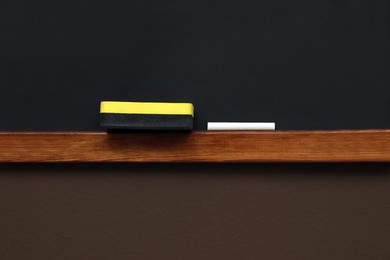 Photo of Clean blackboard with chalk and duster hanging on brown wall