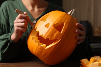 Woman carving pumpkin for Halloween at wooden table, closeup