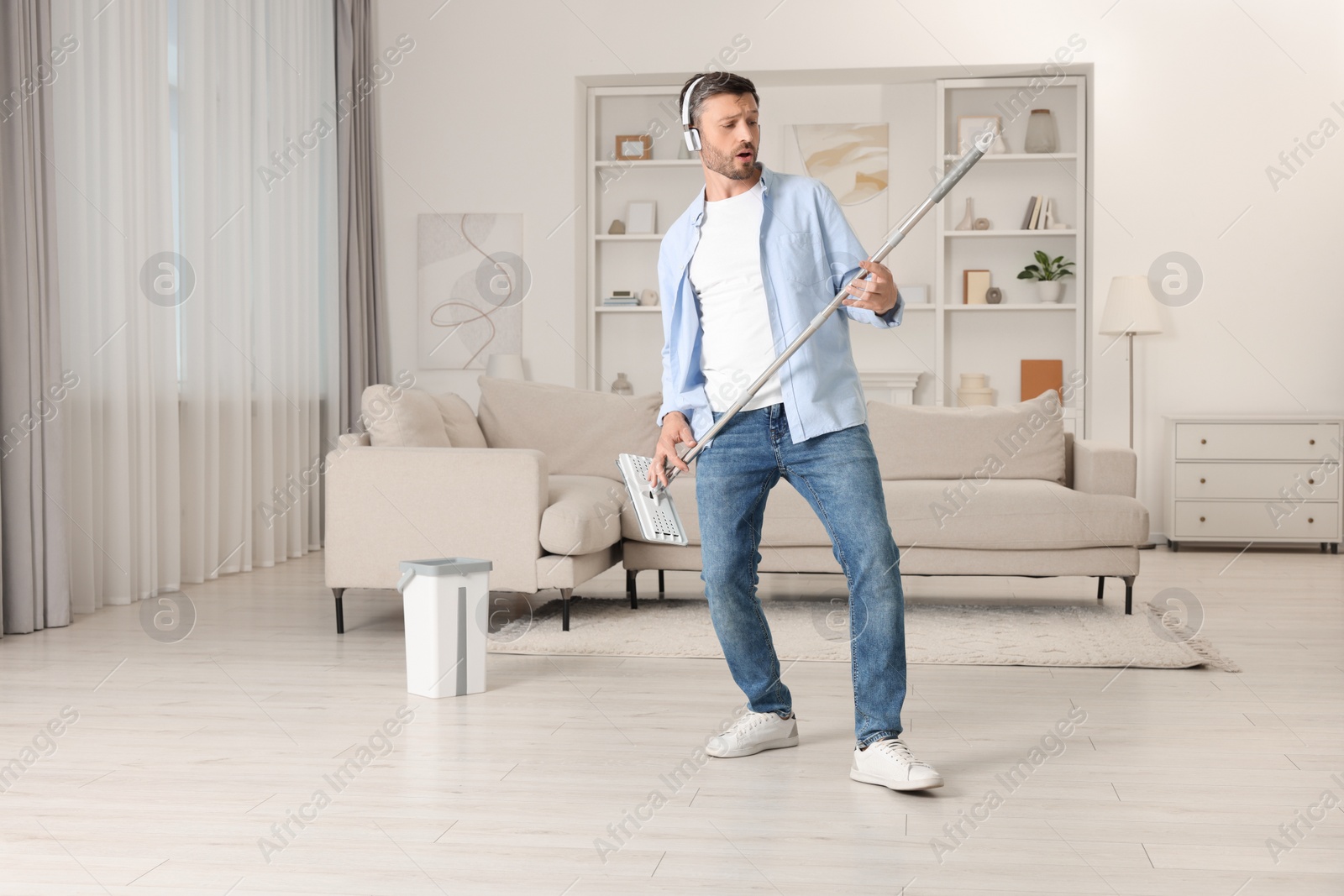 Photo of Happy man in headphones having fun with mop while cleaning at home