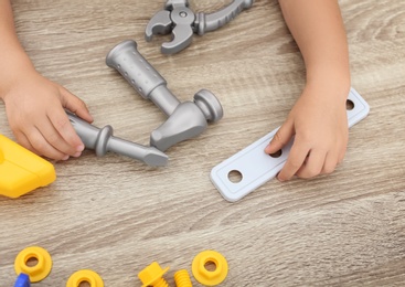 Little boy playing with toy construction tools at wooden table, closeup