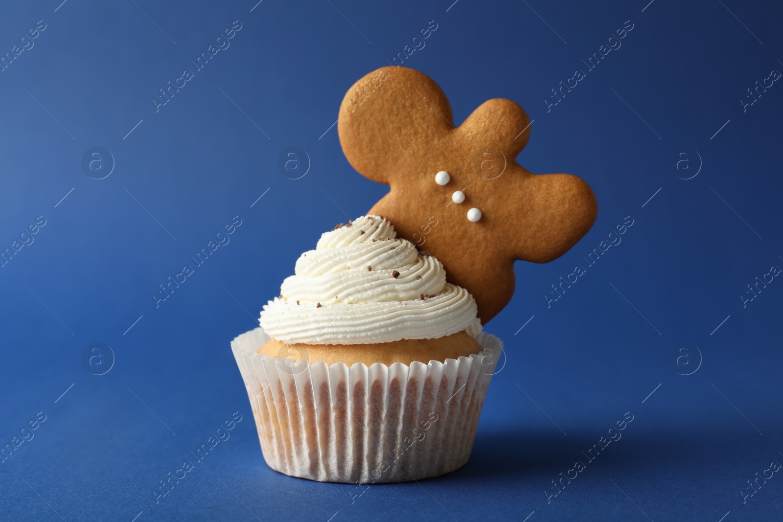 Photo of Tasty Christmas cupcake with cream and gingerbread man cookie on blue background