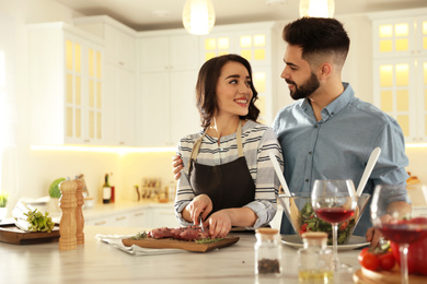 Lovely young couple cooking meat together in kitchen