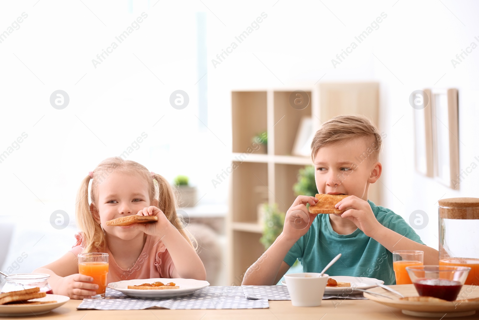 Photo of Adorable little children eating tasty toasted bread with jam at table