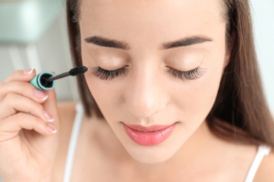 Attractive young woman applying mascara on her eyelashes against blurred background