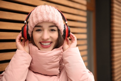 Photo of Young woman listening to music with headphones near wooden wall. Space for text