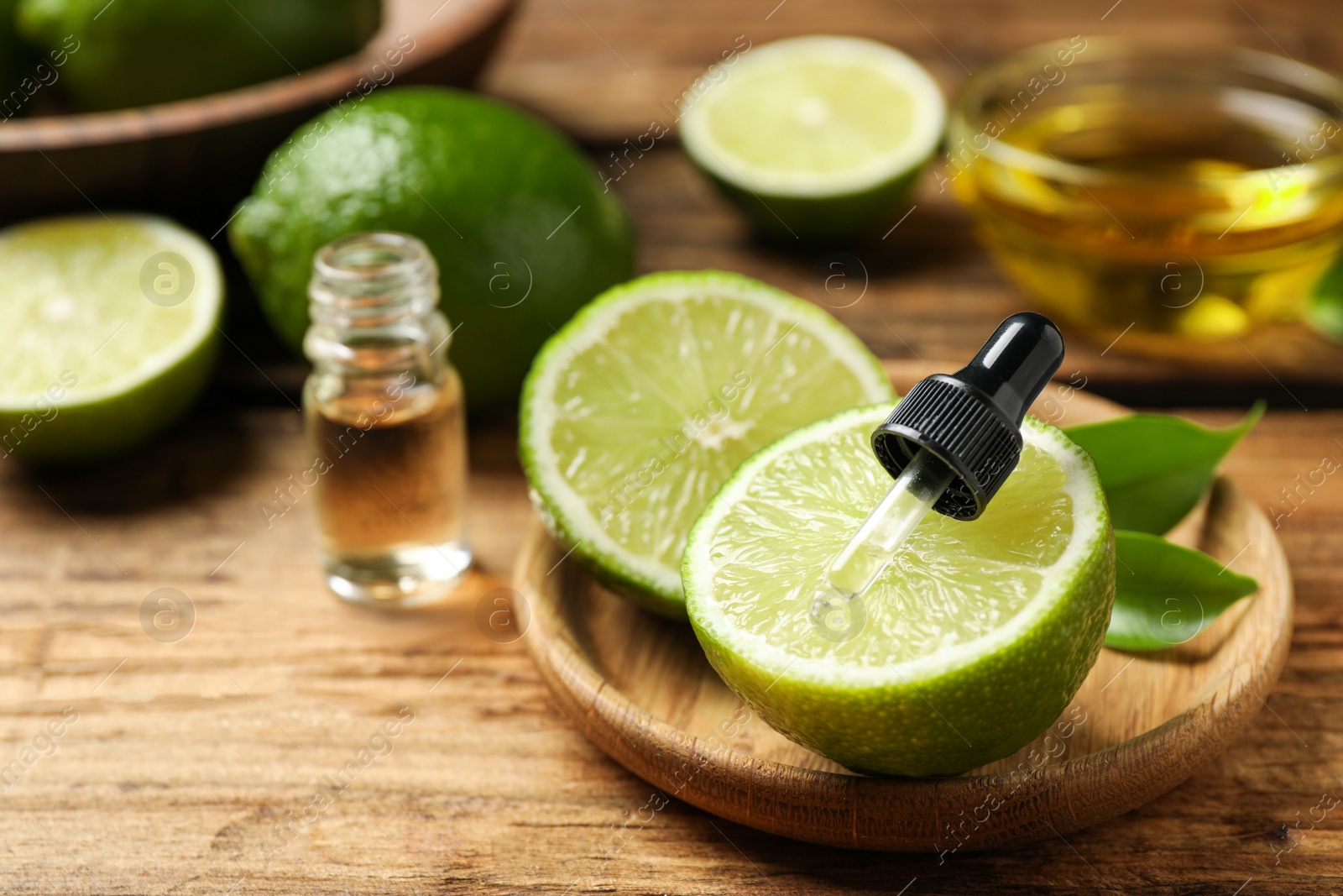 Photo of Dropper with lime essential oil and cut citrus fruit on wooden table