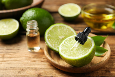 Photo of Dropper with lime essential oil and cut citrus fruit on wooden table