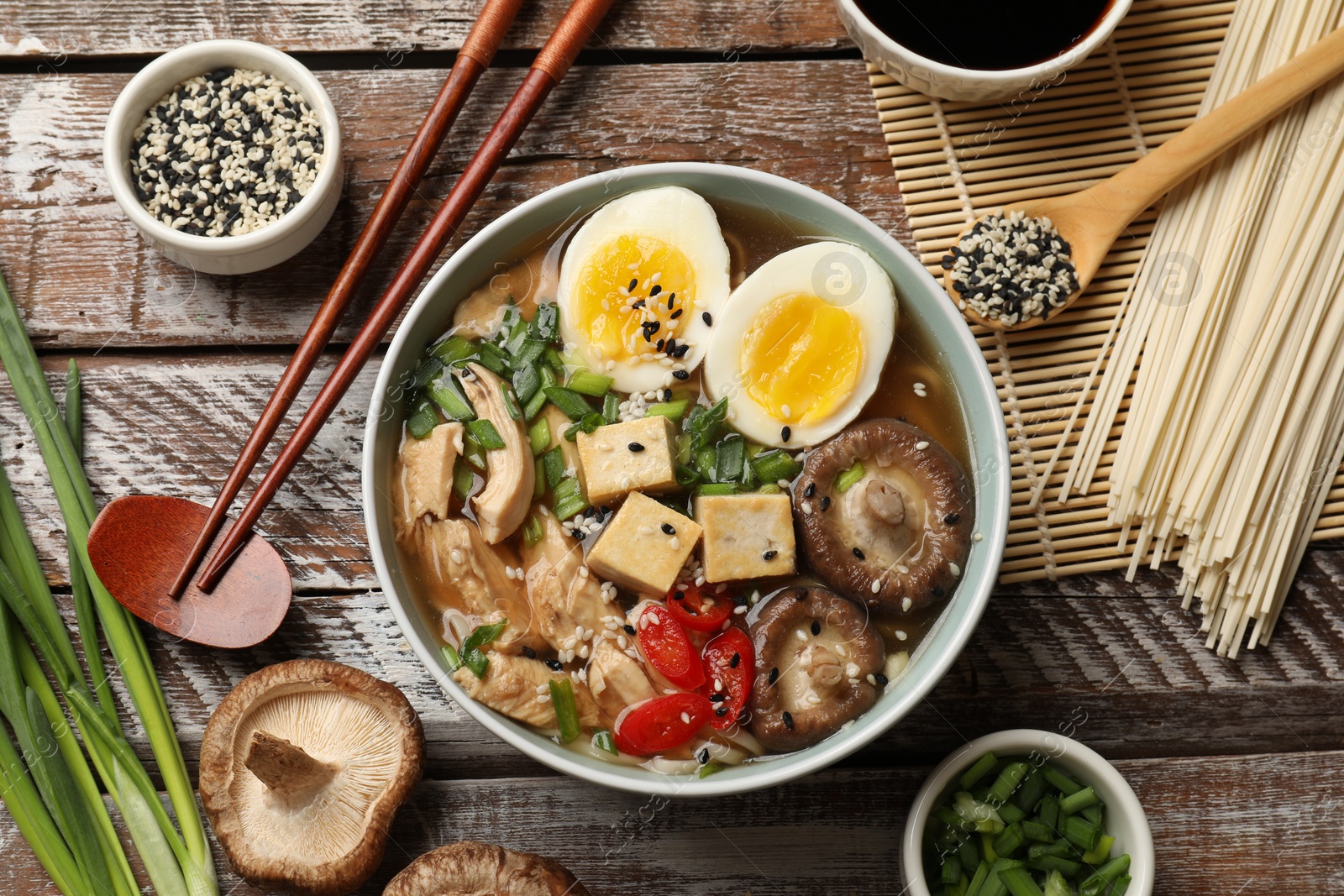 Photo of Noodle soup. Bowl of delicious ramen, ingredients and chopsticks on wooden table, flat lay