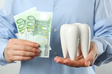 Photo of Woman holding ceramic model of tooth and euro banknotes on light background, closeup. Expensive treatment