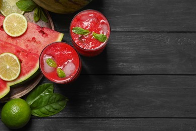 Photo of Glasses of delicious fresh watermelon juice, lime, mint and ice on black wooden table, flat lay. Space for text