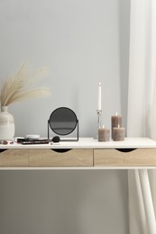 Photo of Dressing table with mirror, cosmetic products and burning candles in makeup room