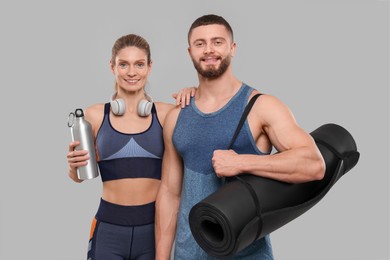 Photo of Athletic people with headphones, thermo bottle and fitness mat on grey background