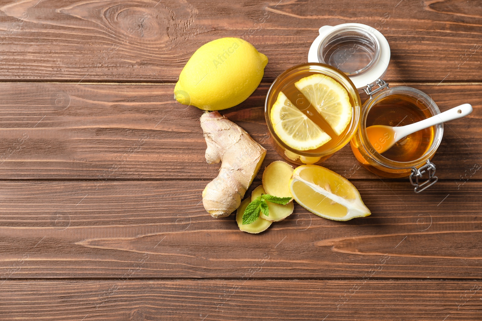 Photo of Glass with hot tea, lemon and ginger as cold remedies on wooden table, top view