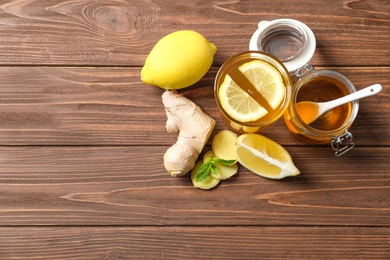 Glass with hot tea, lemon and ginger as cold remedies on wooden table, top view