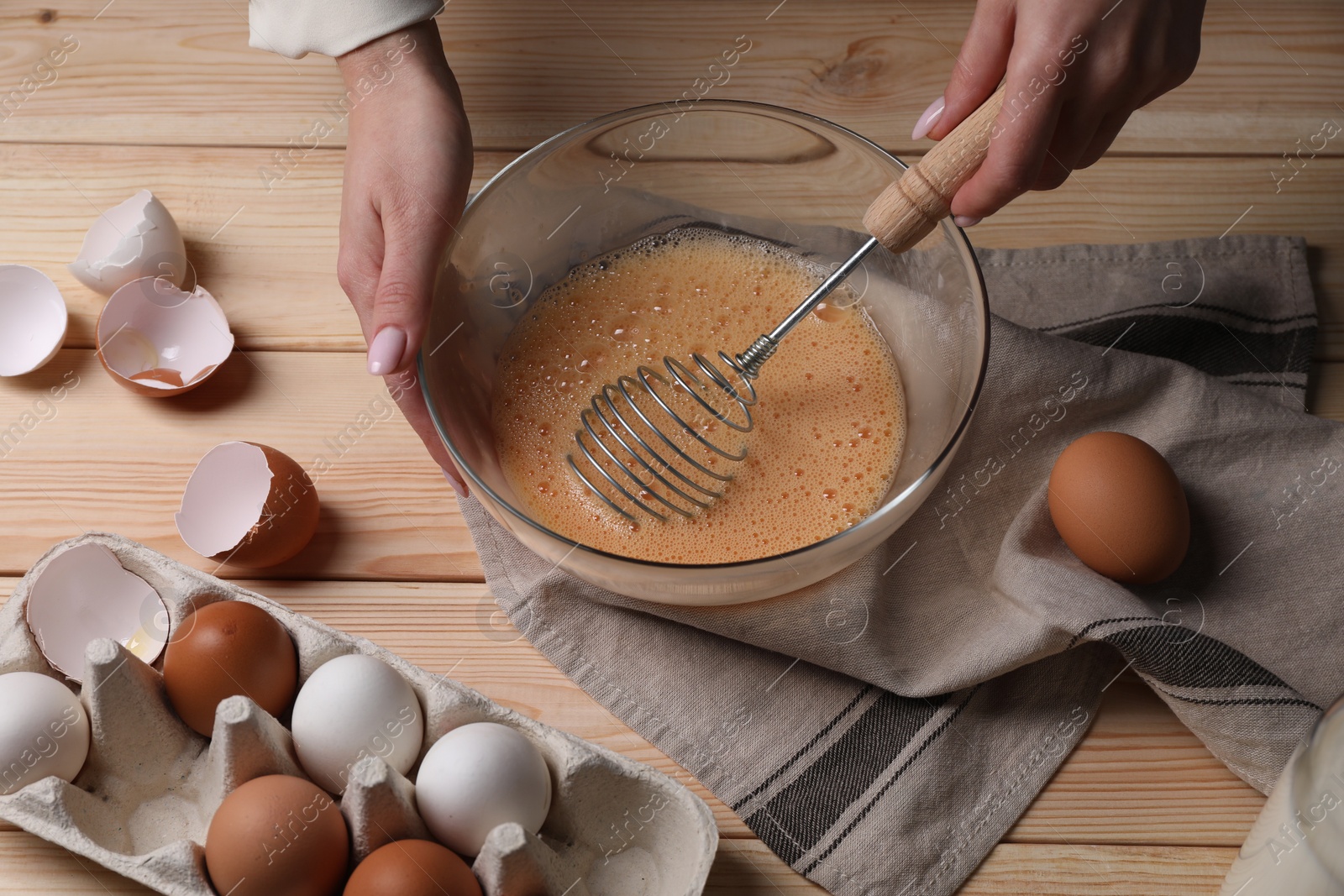 Photo of Woman whisking eggs in bowl at wooden table, above view