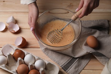 Woman whisking eggs in bowl at wooden table, above view