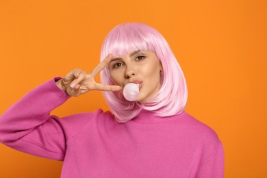 Photo of Beautiful woman blowing bubble gum and showing V-sign on orange background