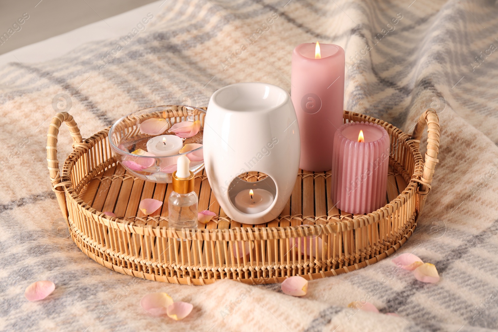 Photo of Wicker tray with aroma lamp, bottle of oil and burning candles on bed