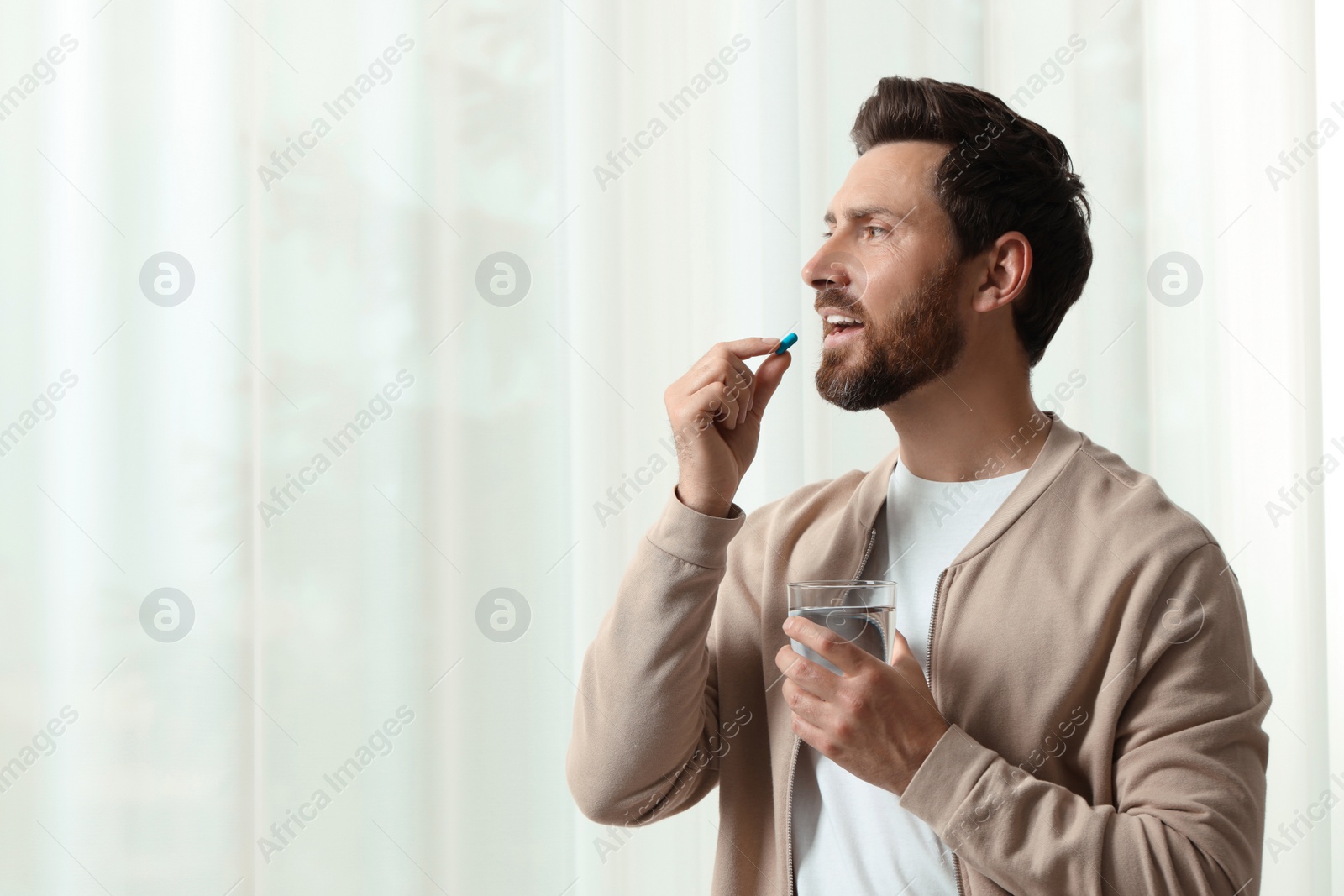 Photo of Handsome man with glass of water taking pill indoors, space for text
