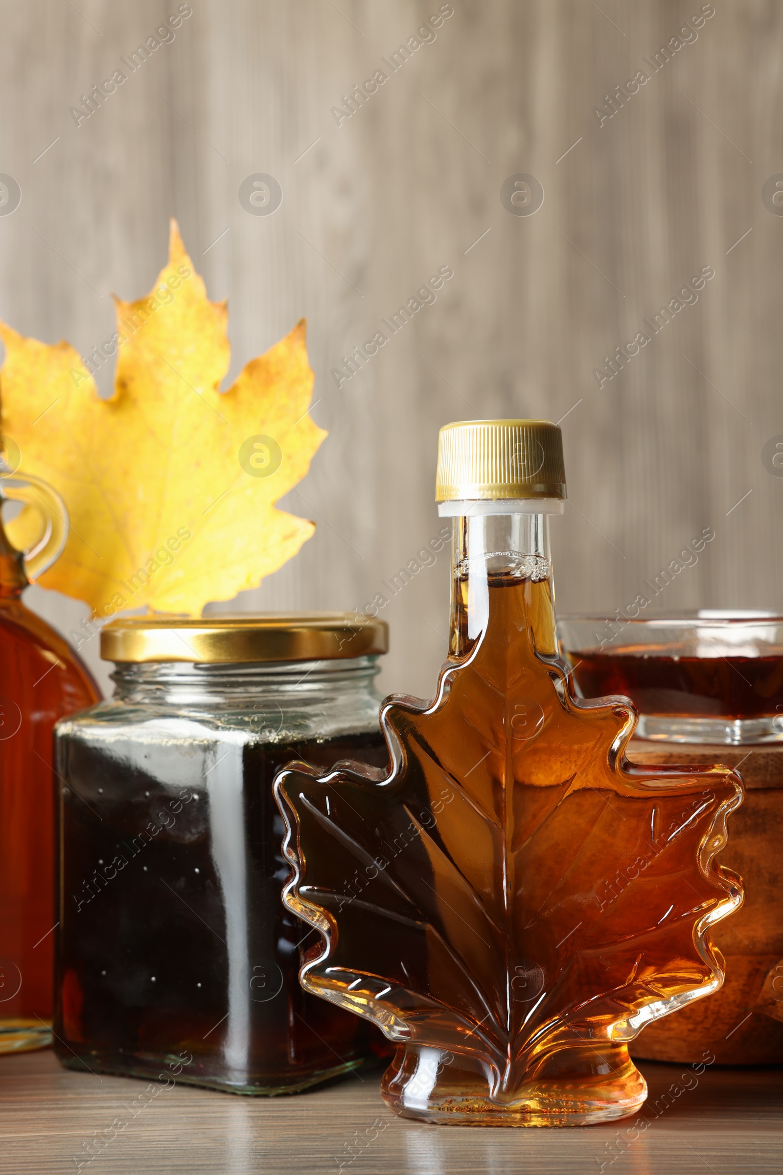 Photo of Bottle and jars of tasty maple syrup on wooden table