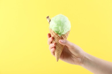 Photo of Woman holding waffle cone with cotton candy on yellow background, closeup