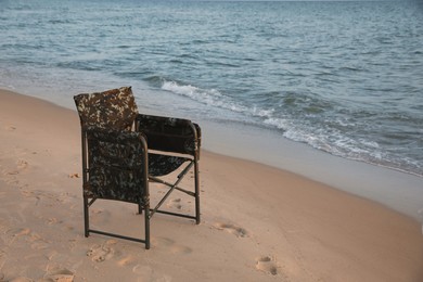Photo of Camping chair on sandy beach near sea, space for text