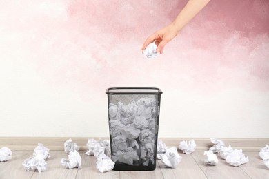 Photo of Woman throwing crumpled paper ball into basket near pink wall, closeup