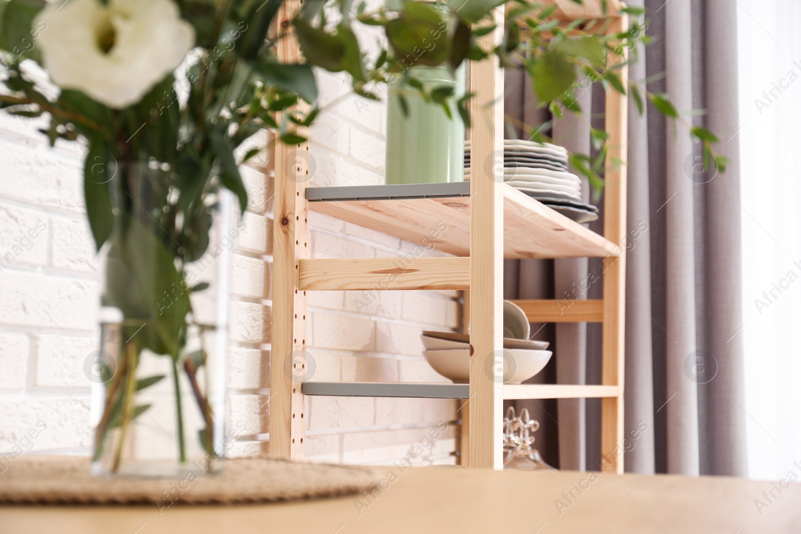 Photo of Wooden shelving unit with tableware indoors. Kitchen interior