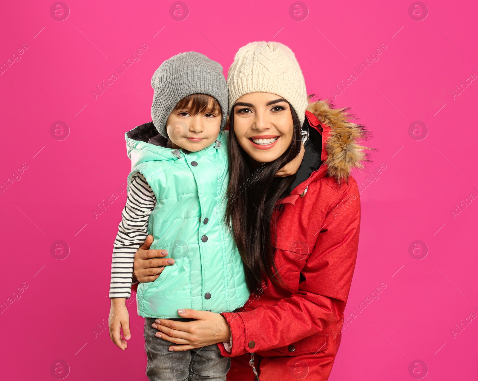 Photo of Happy mother and son in warm clothes on pink background. Winter vacation