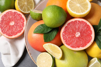 Photo of Different fresh citrus fruits and leaves on grey table, top view