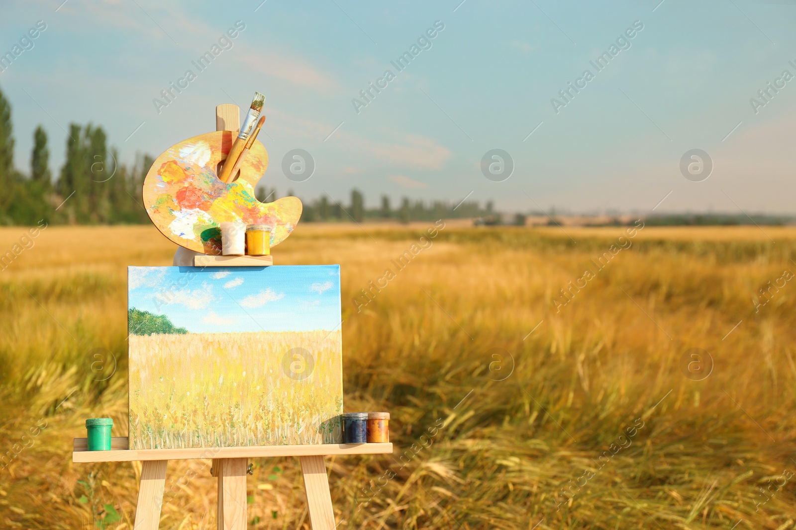 Photo of Wooden easel with beautiful picture and painting equipment in field. Space for text