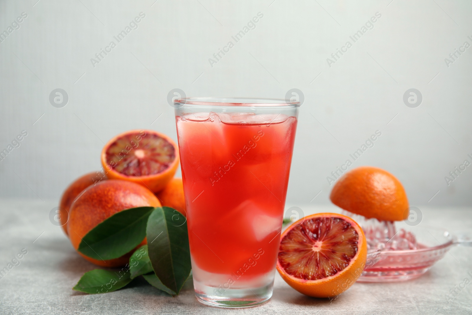 Photo of Tasty sicilian orange juice with ice cubes in glass, fruits and squeezer on light grey table