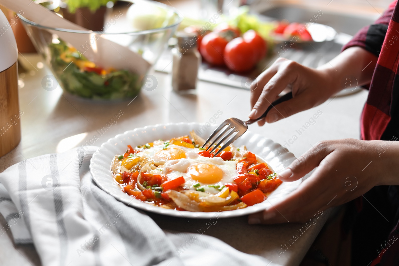 Photo of Woman eating tasty fried eggs with vegetables at table indoors, closeup