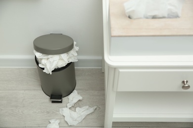 Photo of Used paper tissues in trash can near table indoors