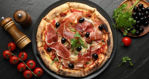 Photo of Tasty pizza with cured ham, olives, tomatoes and parsley on black table, top view