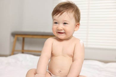 Photo of Cute little baby with moisturizing cream on body at home