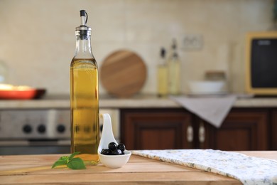 Photo of Bottle of cooking oil, olives and basil on wooden table in kitchen, space for text
