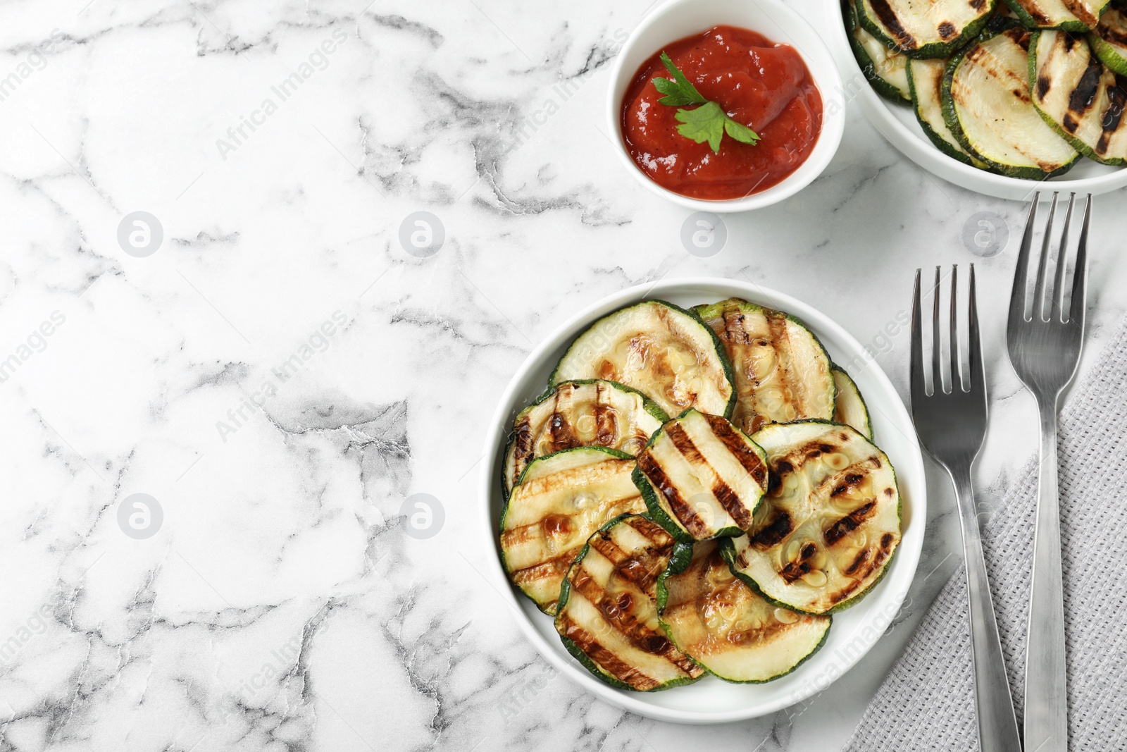 Photo of Grilled zucchini slices served with sauce on white marble table, flat lay. Space for text