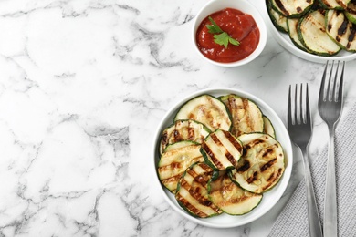 Photo of Grilled zucchini slices served with sauce on white marble table, flat lay. Space for text